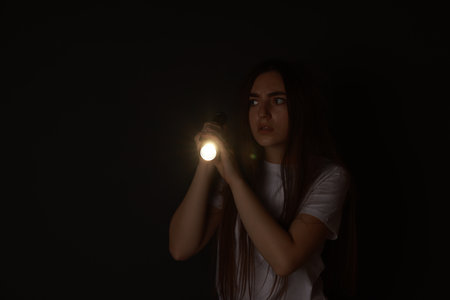 Fear of darkness. Scared young woman with flashlight indoors at night