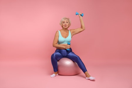 Senior woman exercising with fitness mat and dumbbells on pink backgroundの写真素材