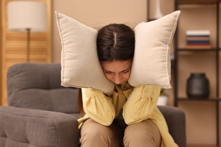 Annoyed woman covering her ears with pillows due to loud sound at homeの写真素材