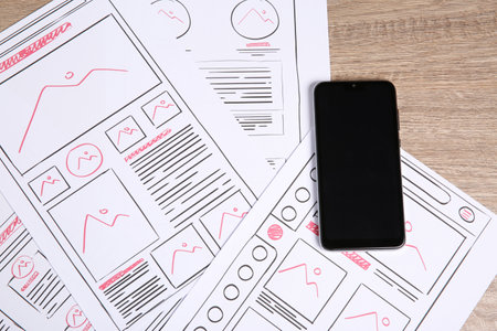 Developing UI design. Sketches of website wireframes and smartphone on wooden table, top viewの写真素材