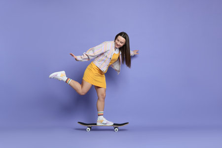 Smiling woman riding skateboard on violet background. Space for textの写真素材