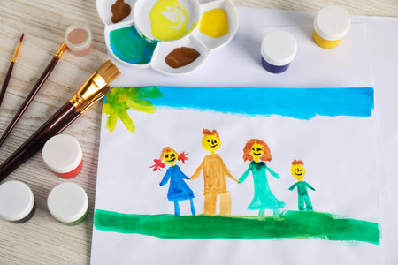 Child's drawing of happy family and supplies on wooden table, top viewの写真素材