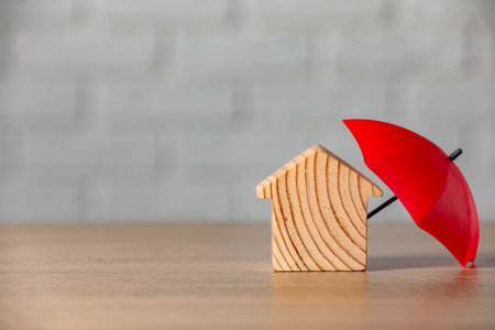 Property insurance. Wooden house figure and small umbrella on table, space for textの写真素材