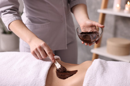 Chocolate body wrap. Spa worker applying mask onto woman's belly in salon, closeupの写真素材