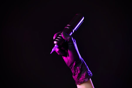 Professional artist holding tattoo machine on black background in color lights, closeupの写真素材