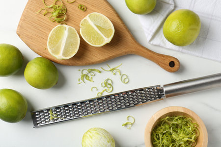 Lime zest, fresh fruits and grater on white marble table, flat layの写真素材