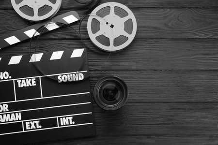 Movie clapper, film reels and camera lens on black wooden table, flat lay. Space for textの写真素材