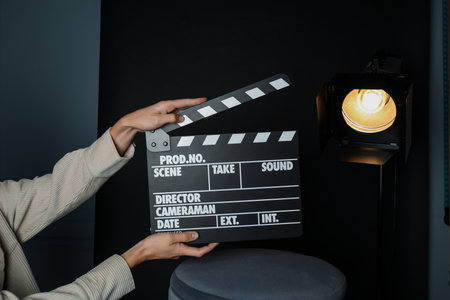 Woman with clapperboard near spotlight on black background, closeupの写真素材