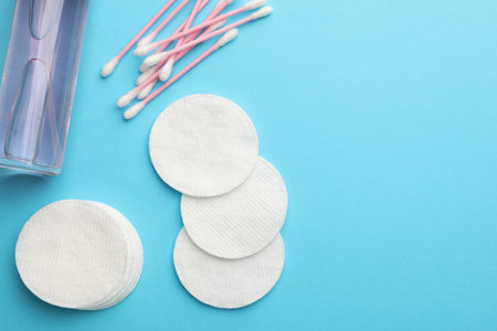 Cotton pads, bottle of cosmetic product and swabs on light blue background, flat lay. Space for textの写真素材