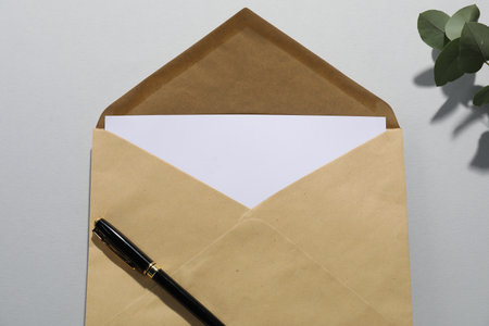 Kraft paper envelope with letter, pen and eucalyptus branch on grey background, above view. Mockup for designの写真素材