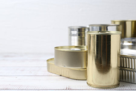 Many closed tin cans on white wooden table, closeup. Space for textの写真素材