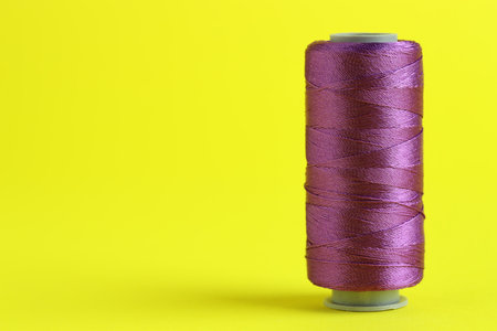 Spool of purple sewing thread on yellow background, space for textの写真素材