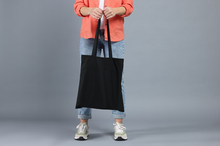 Woman with blank black shopper bag on grey background, closeup. Mockup for design