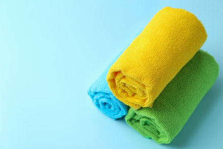 Rolled different microfiber cloths on light blue background, closeup. Space for textの写真素材
