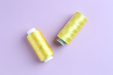 Spools of yellow sewing threads on lilac background, top view