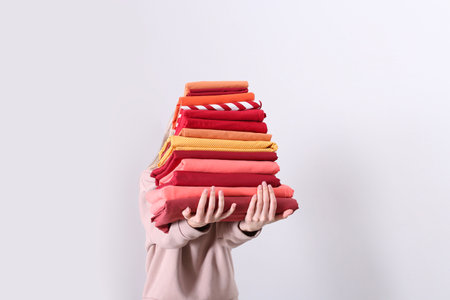 Woman holding stack of clean bed linens on light backgroundの写真素材