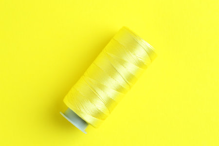 Spool of bright sewing thread on yellow background, top view