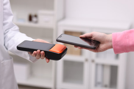 Woman paying with smartphone via terminal against blurred background, closeup