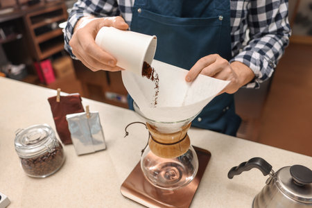Barista pouring ground coffee into glass coffeemaker with paper filter at table in cafe, closeupの写真素材