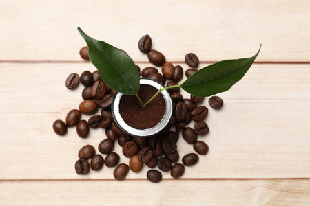 Coffee capsule with seedling and beans on light wooden table, flat lay