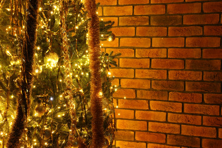 Shiny tinsels, baubles and festive lights on Christmas tree near brick wall. Space for textの写真素材