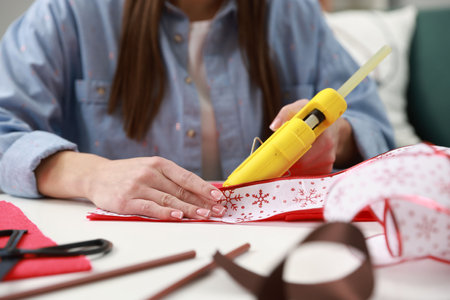 Woman with hot glue gun making craft at table indoors, closeupの写真素材