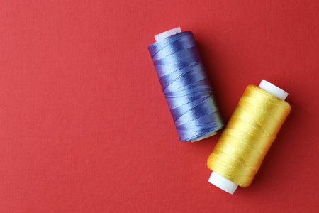 Spools of colorful sewing threads on red background, flat lay. Space for text