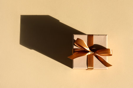 Beautiful gift box with golden bow casting shadow of house on beige background, top view. Space for textの写真素材