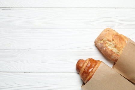 Paper bag with fresh baguette and croissant on white wooden table, top view. Space for textの写真素材