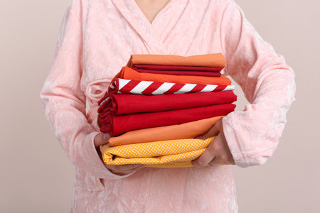 Woman holding stack of clean bed linens on beige background, closeupの写真素材
