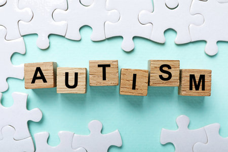 Word Autism made with wooden cubes and puzzle pieces on light blue background, flat layの写真素材