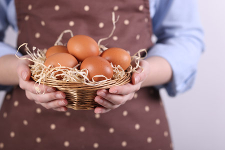 Woman with basket of raw eggs on light background, closeupの写真素材