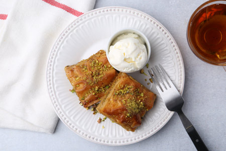 Delicious baklava with crushed nuts and ice cream served on gray table, flat lay
