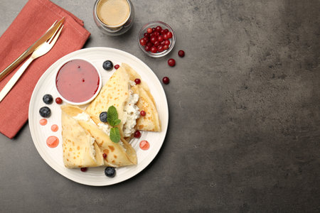 Delicious crepes with cottage cheese, jam, redcurrants and blueberries served on gray table, flat lay. Space for textの写真素材