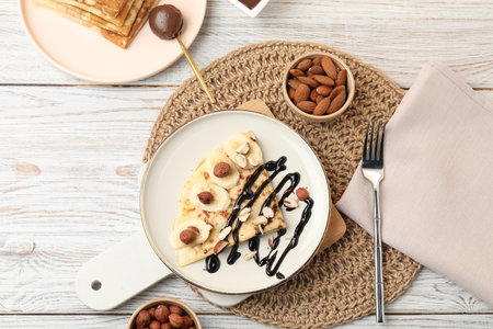Delicious crepes served with chocolate sauce and nuts on wooden table, flat layの写真素材
