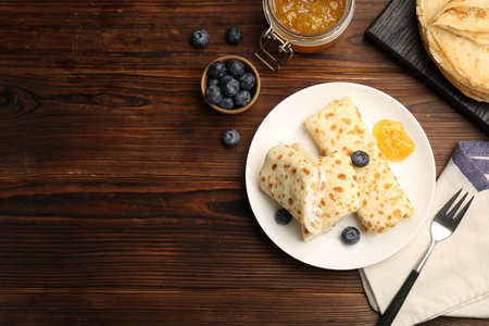 Delicious crepes with cottage cheese, jam and blueberries served on wooden table, flat lay. Space for textの写真素材