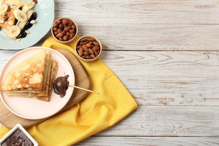 Delicious crepes served with chocolate paste and nuts on wooden table, flat lay. Space for textの写真素材