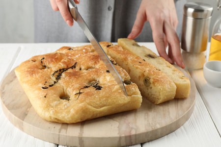 Woman cutting delicious focaccia bread at white wooden table, closeupの写真素材