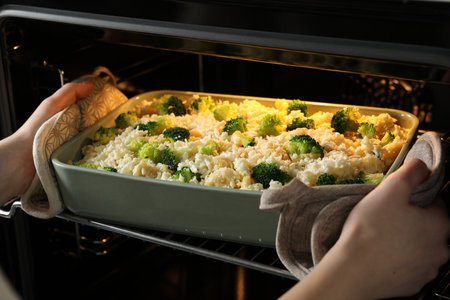 Woman putting dish with uncooked pasta casserole into oven indoors, closeupの写真素材