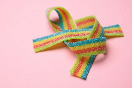Tasty rainbow sour belts on pink background, closeup