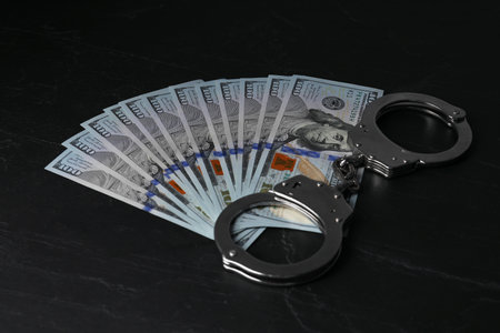 Corruption. Dollar banknotes and handcuffs on black tableの写真素材