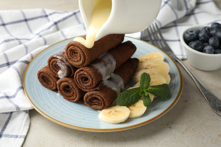 Pouring milk onto chocolate crepes with banana on light table, closeupの写真素材