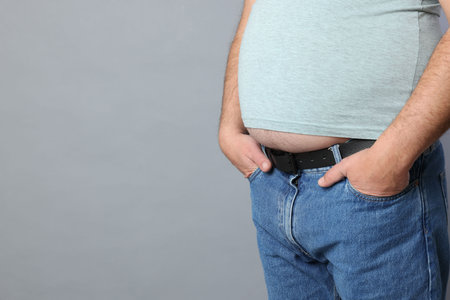 Overweight man in tight t-shirt on gray background, closeup. Space for text