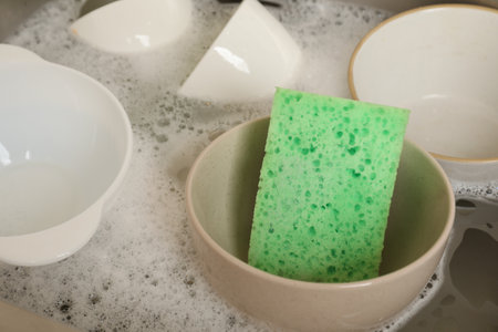 Green sponge, dishes and foam in sink, closeup