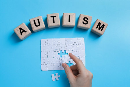 Word Autism made of wooden cubes. Woman solving puzzle on light blue background, top viewの写真素材