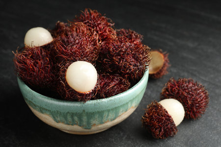 Delicious ripe rambutans in bowl on black table, closeupの写真素材
