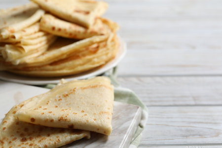 Many tasty crepes on white wooden table, closeup. Space for text