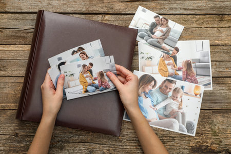 Woman with different photos and photo album at wooden table, top view