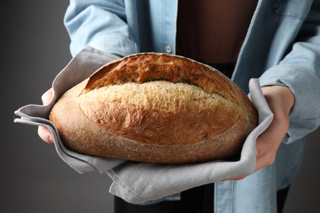 Woman with loaf of freshly baked bread on gray background, closeup