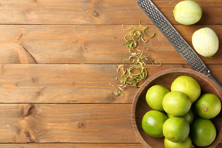 Lime zest, grater and fresh fruits on wooden table, flat lay. Space for text